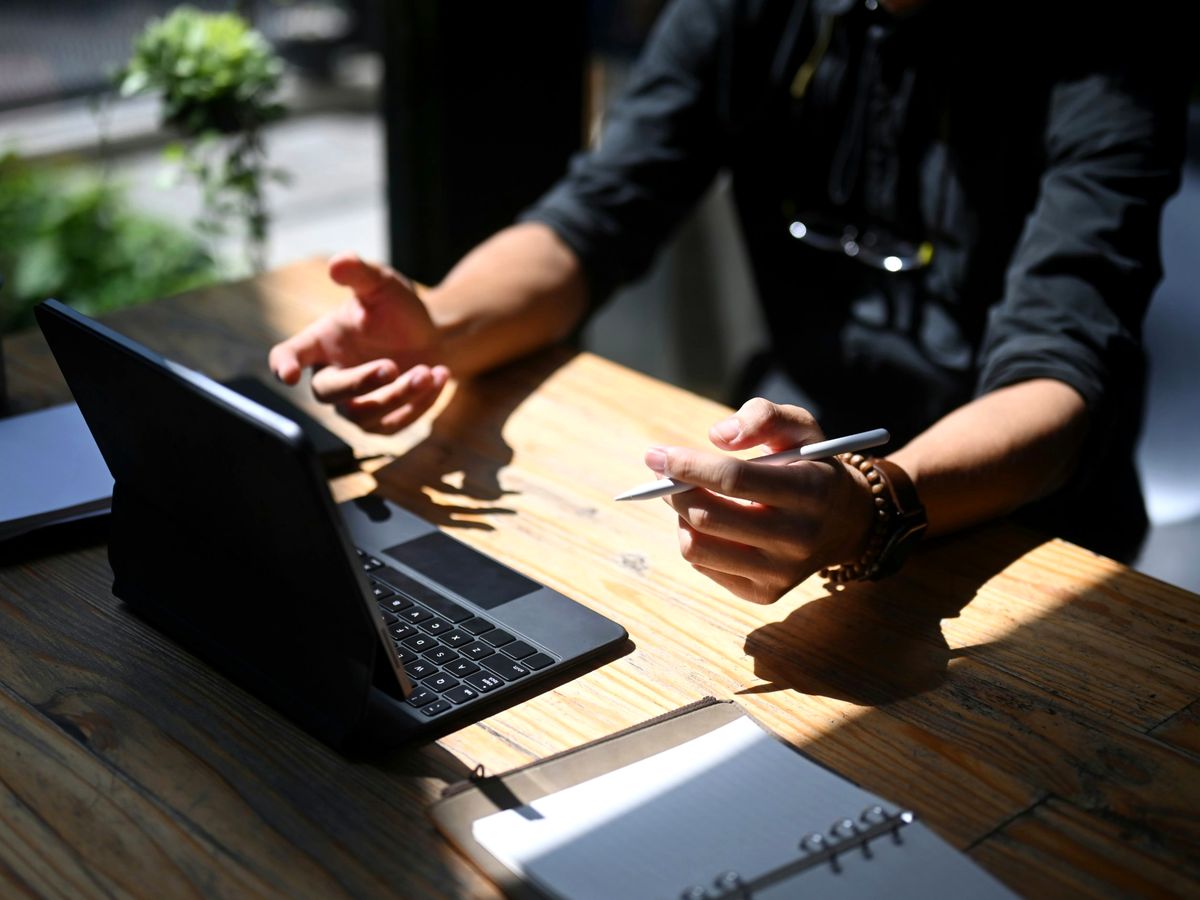 Videóhívás laptopon, egy férfi a kezével magyaráz, kezében toll
